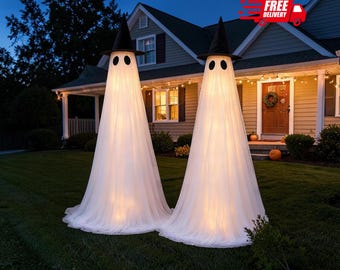 Puede incluir: Dos decoraciones de fantasmas iluminadas de gran tamaño sobre un césped. Cada figura está cubierta con tela blanca, lleva un sombrero de bruja negro puntiagudo y tiene dos ojos oscuros ovalados. La luz interna crea un brillo cálido.
