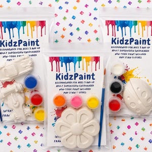 May include: Three clear plastic bags labeled KidzPaint containing white plaster shapes, small paint pots in various colors, and a blue paintbrush. The labels state recommended for ages 3 and up, adult supervision encouraged, non-toxic paint included, and may stain clothes.