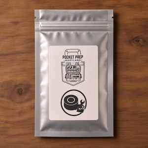 May include: A silver metallic resealable pouch featuring a white rectangular label. The label displays a black graphic of a pocket with the text POCKET PREP MARYLAND and PPMD, followed by a circular icon containing a roll of tape and a wrench.