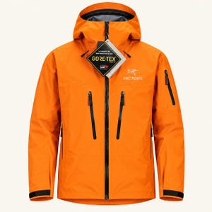 May include: A bright orange hooded jacket featuring a full-length black front zipper, two vertical chest pockets with black zippers, and a small sleeve pocket. The Arc'teryx logo is printed on the chest, and a Gore-Tex product tag is attached.