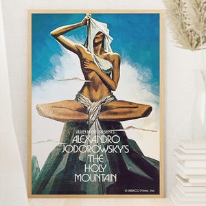 May include: A rectangular movie poster for The Holy Mountain featuring a figure in a seated pose atop a dark mountain against a blue sky. The text reads Allen Klein Presents Alexandro Jodorowsky's The Holy Mountain and ABKCO Films, Inc.
