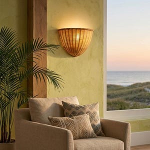 May include: A semi-circular wall sconce crafted from light brown woven rattan, featuring a flared top edge and a tapered base. The fixture emits a warm, soft glow against the wall, showcasing a natural texture and a structured, fan-like design.