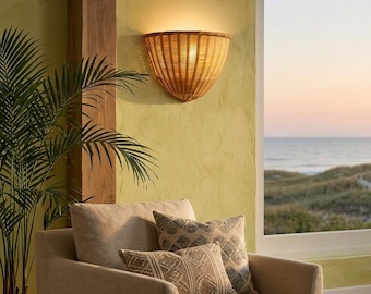 May include: A semi-circular wall sconce crafted from light brown woven rattan, featuring a flared top edge and a tapered base. The fixture emits a warm, soft glow against the wall, showcasing a natural texture and a structured, fan-like design.