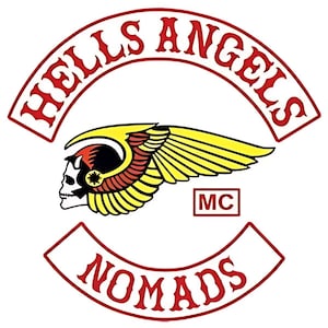 May include: A circular emblem featuring the text HELLS ANGELS in red arched lettering at the top and NOMADS in red arched lettering at the bottom. In the center, a white skull with a winged helmet in yellow and red, with the letters MC in a box.