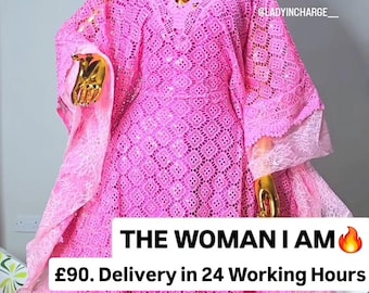 Può includere: Un abito caftano in pizzo rosa acceso con un intricato motivo geometrico, scollo a V e copricapo abbinato. Il capo è esposto su un manichino dorato. Il testo sull'immagine recita: THE WOMAN I AM.