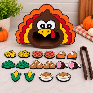 May include: A brown turkey-shaped container with a colorful orange, yellow, and red tail, accompanied by various food-shaped game pieces including macaroni, pies, green beans, rolls, meat, corn, and mashed potatoes, plus brown plastic tongs.