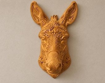 Può includere: Una scultura da parete raffigurante una testa di asino in tinta unita giallo senape. L'oggetto presenta intricati motivi a vortice in rilievo e linee incise che coprono l'intera superficie, mettendo in risalto le orecchie, gli occhi e il muso.