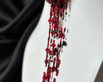 May include: A beaded choker necklace featuring a dense collar of small red and black beads with long, cascading vertical strands of varying lengths. The strands are composed of faceted red and black beads strung on clear filament.