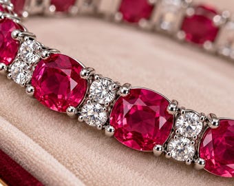 Puede incluir: Una pulsera de tono plateado con un patrón repetitivo de grandes piedras preciosas de color rojo vibrante en talla cojín, alternadas con pares de pequeñas piedras redondas y transparentes facetadas en metal.