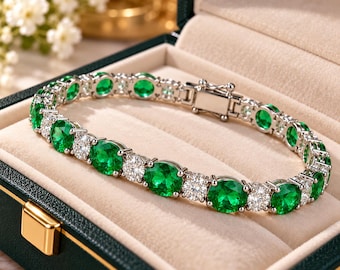 Puede incluir: Una pulsera de tenis en tono plateado con piedras redondas de color verde vibrante y piedras blancas transparentes alternadas, asegurada con un cierre de caja, presentada en un joyero verde oscuro con forro de terciopelo beige.
