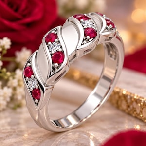 Könnte beinhalten: Ein silberfarbener Ring mit einer Reihe abwechselnd geschliffener roter Rubine und klarer weißer Diamanten, die in ein poliertes Metallband eingefasst sind. Das Design umfasst glatte, geschwungene Metallsegmente zwischen den Steinreihen.