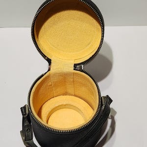 May include: A black, round, open watch case with a yellow interior. The case has a zipper closure and a small handle. The interior has a circular cushion to hold a watch.