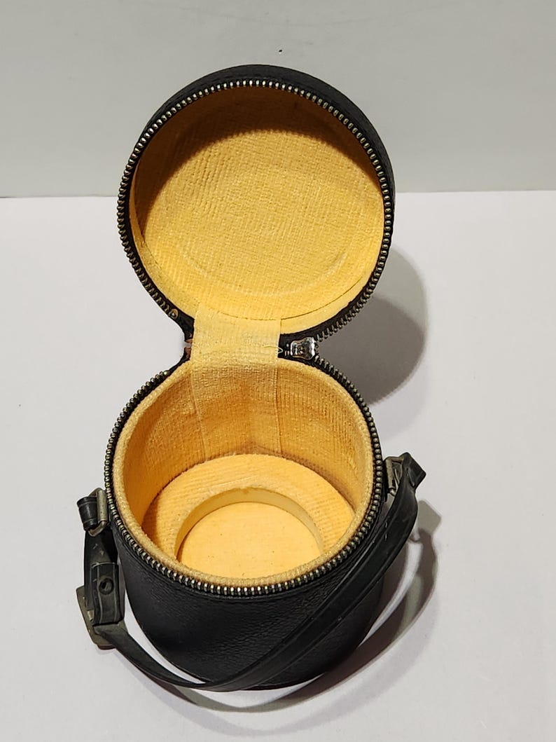 May include: A black, round, open watch case with a yellow interior. The case has a zipper closure and a small handle. The interior has a circular cushion to hold a watch.