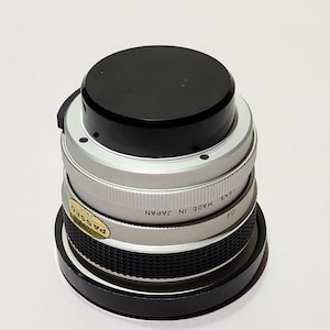 May include: A silver and black camera lens with a black top. The lens has a ridged silver band and a sticker that reads "PASSED". The text "MADE IN JAPAN" is also visible on the lens.