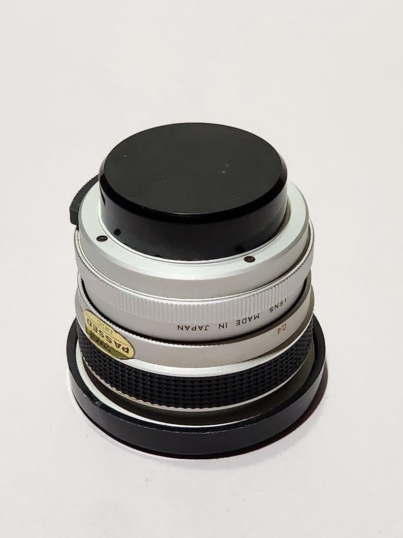 May include: A silver and black camera lens with a black top. The lens has a ridged silver band and a sticker that reads "PASSED". The text "MADE IN JAPAN" is also visible on the lens.