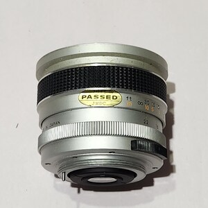 May include: Silver and black camera lens with a ridged focus ring and aperture settings. The lens has a "PASSED" sticker and markings in feet and inches. The lens is marked "MADE IN JAPAN".