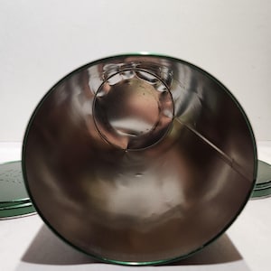 以下が含まれることがあります： 緑色の縁と蓋が付いた、開いた円筒形の金属容器。内側は光沢のある銀色です。容器は空で、スズまたは同様の金属でできているようです。蓋は背景に見えます。