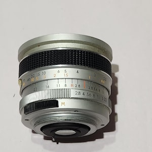 May include: A silver camera lens with black textured grip and various markings. The lens has a series of numbers and letters, including "M" and "2.8 4 5.6 8 11 16 22". The lens is designed for photography.