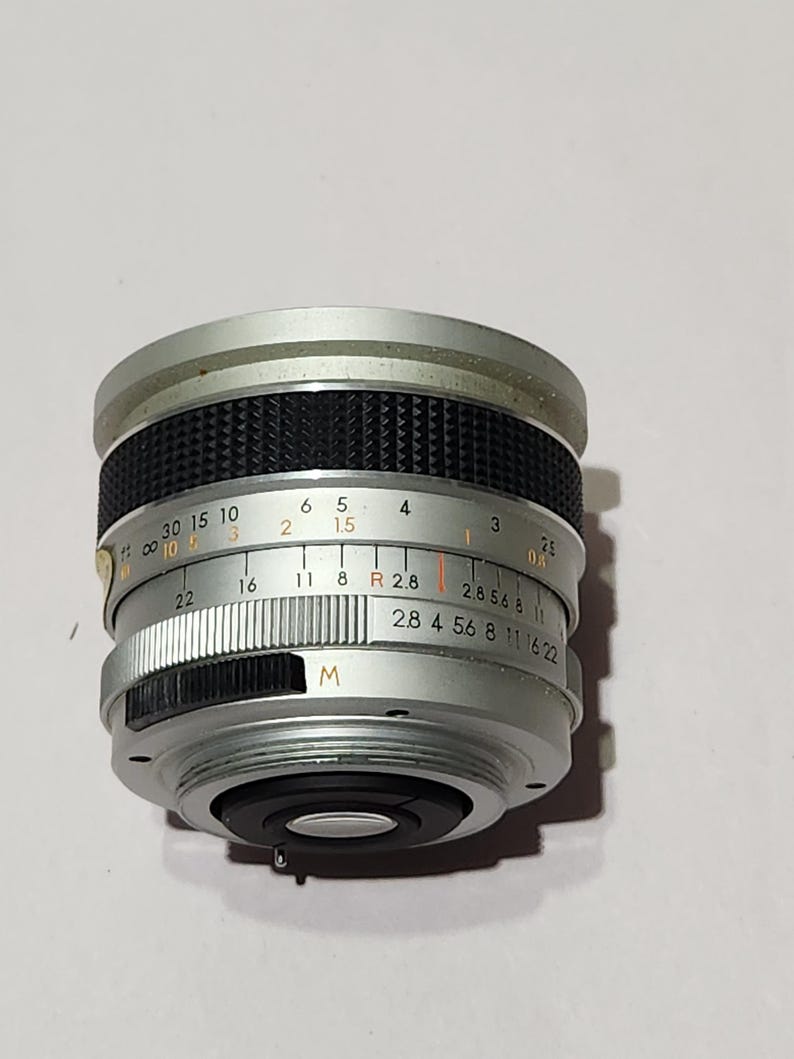 May include: A silver camera lens with black textured grip and various markings. The lens has a series of numbers and letters, including "M" and "2.8 4 5.6 8 11 16 22". The lens is designed for photography.