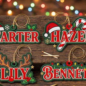 May include: Four custom Christmas ornaments with gold hanging strings. The ornaments feature the names Carter, Hazel, Lily, and Bennett in red lettering on green backgrounds, decorated with Santa hats, holly, a candy cane, and lights.