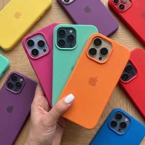 Puede incluir: Una colección de fundas de silicona para smartphone en varios colores sólidos, incluyendo amarillo, morado, rojo, rosa, verde menta, naranja y azul. Cada funda presenta un recorte cuadrado para la cámara y un logotipo de Apple en la parte trasera.