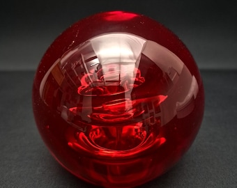 May include: A spherical red glass paperweight featuring a clear, smooth surface and a complex, swirling internal structure that creates depth and light refraction within the solid, transparent red orb.