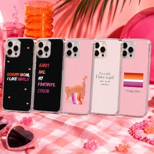 Könnte beinhalten: Fünf transparente Smartphone-Hüllen in einer Reihe. Die erste ist schwarz mit einem Gitter und dem Text SORRY MOM, I LIKE GIRLS. Die zweite ist schwarz mit dem Text GIRLS ARE MY FAVORITE COLOR. Die dritte ist rosa mit einer Katze, die eine lesbische Flagge hält. Die vierte ist hellrosa mit dem Text I'm a girl. I love a girl And i'm ok with that. Die fünfte ist rosa mit einer lesbischen Flagge und dem Text I'm gay, bitch.