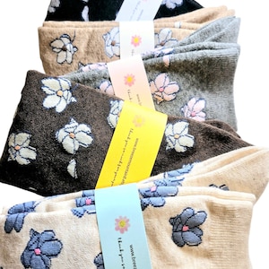 May include: A stack of five pairs of socks with floral patterns. The socks are in various colours, including black, brown, beige, grey, and white. Each pair has a different floral design. The socks are packaged with a small tag that says "Thank you so much for your purchase!" and "www.breezemountain8.etsy.com".