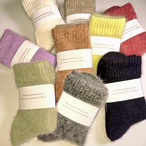 May include: A collection of fuzzy socks in various colors including cream, beige, red, lavender, lime green, tan, sage green, charcoal gray, and black. Each pair is wrapped in a white paper band printed with the text breezemountain.etsy.com.