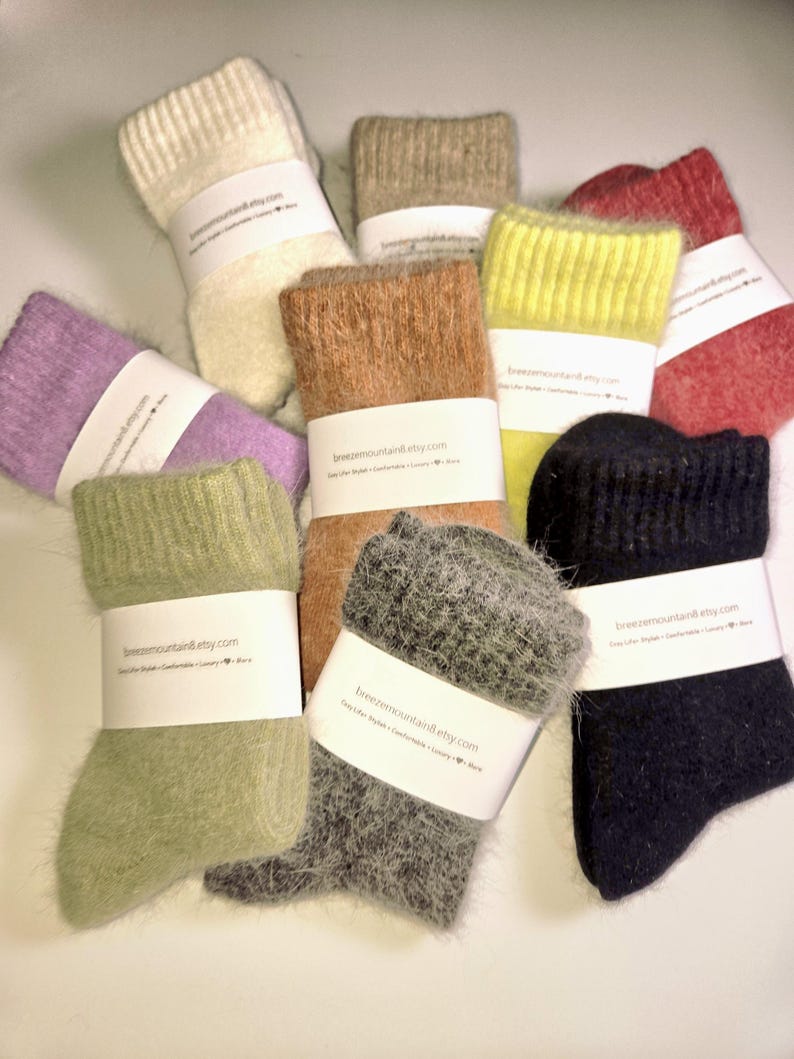 May include: A collection of fuzzy socks in various colors including cream, beige, red, lavender, lime green, tan, sage green, charcoal gray, and black. Each pair is wrapped in a white paper band printed with the text breezemountain.etsy.com.