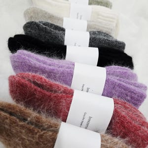 May include: A stack of fuzzy, ribbed knit socks in various colors including lime green, cream, gray, charcoal, black, purple, red, and brown. Each pair is secured with a white paper band featuring the text breezemo Cozy Life Stylish.