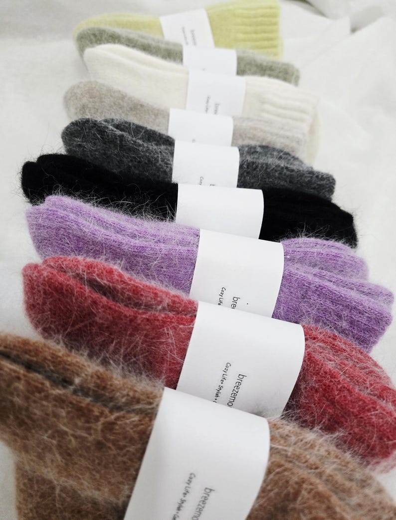 May include: A stack of fuzzy, ribbed knit socks in various colors including lime green, cream, gray, charcoal, black, purple, red, and brown. Each pair is secured with a white paper band featuring the text breezemo Cozy Life Stylish.