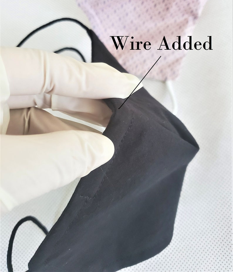 May include: A black face mask with a wire added to the top edge. The wire is visible through the fabric. The mask is being held by a gloved hand.