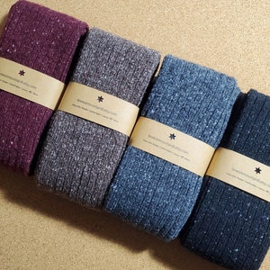 Op de afbeelding: Vier paar gevouwen gebreide sokken in tinten bordeauxrood, grijs, blauw en marineblauw. Elk paar is verpakt met een bruine papieren band bedrukt met de tekst "breezemountain8.etsy.com". De sokken hebben een geribbelde textuur en een gespikkeld patroon.