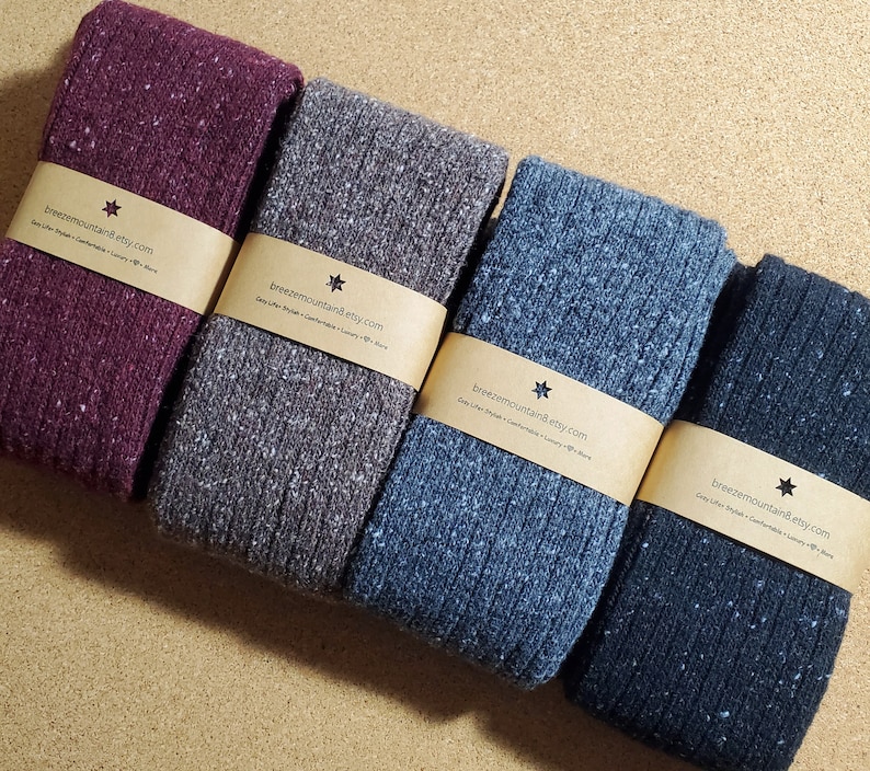 Op de afbeelding: Vier paar gevouwen gebreide sokken in tinten bordeauxrood, grijs, blauw en marineblauw. Elk paar is verpakt met een bruine papieren band bedrukt met de tekst "breezemountain8.etsy.com". De sokken hebben een geribbelde textuur en een gespikkeld patroon.