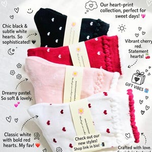 May include: A collection of heart-print socks in black, red, pink, and white. Each pair features a different heart pattern and trim. The image includes text that says "Check out our new styles! Shop link in bio!"