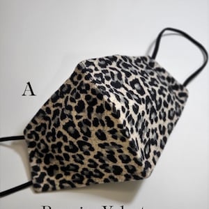 May include: A black and white leopard print face mask made of velvet. The mask has a black elastic band and the text "Premier Velvet" is printed below the mask.