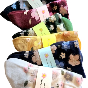 May include: A set of six pairs of socks with floral patterns. The socks are in various colors, including black, burgundy, green, yellow, navy blue, and white. Each pair of socks has a small tag attached to it with the text "Thank you so much for your purchase! www.breezemountains.etsy.com".