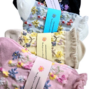 May include: Four pairs of ankle socks in various colors: black, light blue, beige, and pink. Each pair features embroidered floral designs in complementary colors. The socks are bundled with paper bands that include the text "Thank you so much for your purchase."