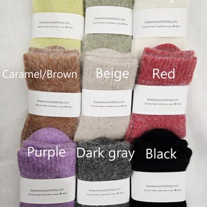 May include: A collection of nine pairs of fuzzy, ribbed knit socks arranged in a grid. The colors include honeydew melon, green, ivory, caramel brown, beige, red, purple, dark gray, and black. Each pair features a white paper band.