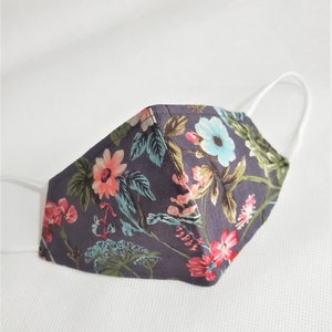 May include: A dark gray face mask with a floral pattern featuring pink, blue, and green flowers. The mask has white elastic ear loops.