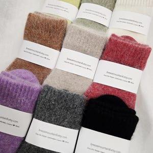 May include: A collection of nine pairs of fuzzy knit socks in various colors including lime green, sage, cream, brown, beige, red, purple, charcoal, and black. Each pair is wrapped in a white paper band labeled breezemountain8.etsy.com.