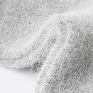 May include: A light gray knit fabric with a soft, fuzzy, and brushed texture. The material features a dense, fibrous surface with long, fine hairs creating a halo effect across the light gray color, showing a folded, layered structure.