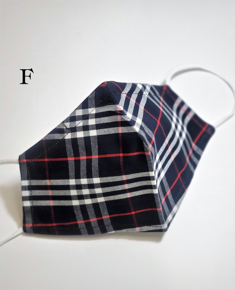 May include: A blue, white, and red plaid face mask with white elastic ear loops. The mask has a sewn seam down the center.