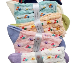 Op de afbeelding: Zes paar kleurrijke sokken met een bloemen- en kersenpatroon. De sokken zijn gemaakt van een zachte, textuurrijke stof en hebben een gerimpelde bovenkant. De sokken zijn verpakt met een wit label waarop "www.breezemountain.com" en "Bedankt voor uw aankoop." staat.