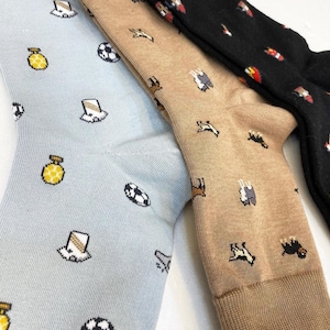 Puede incluir: Tres pares de calcetines con diferentes patrones. Un par es azul claro con un patrón de balones de fútbol, botellas de perfume y sombreros. Otro par es beige con un patrón de caballos y ovejas. El tercer par es negro con un patrón de camiones de bomberos rojos y blancos.