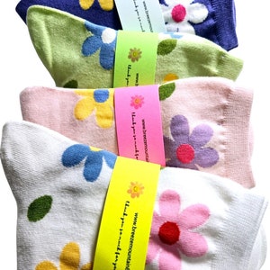 May include: Four pairs of patterned socks in shades of blue, green, pink, and white, each folded and banded. The socks display a floral design with white, blue, yellow, pink, and purple flowers. Each tag has text.