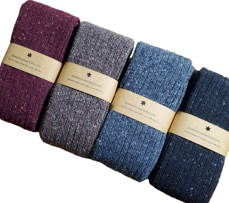 Op de afbeelding: Vier paar gevouwen, geribbelde gebreide sokken in verschillende tinten grijs, blauw en bordeaux. Elk paar is verpakt met een bruine papieren band met de tekst "breezemountain8.etsy.com". De sokken hebben een gespikkeld patroon.