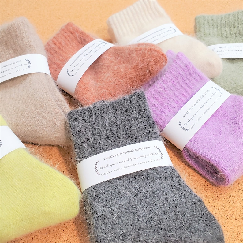 May include: A collection of fuzzy, soft-textured socks in various colors including gray, lavender, peach, beige, cream, green, and yellow. Each pair is wrapped in a white paper band featuring the text www.breezemountain8.etsy.com and thank you so much for your purchase.