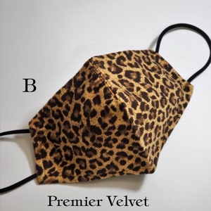 May include: A brown and black leopard print face mask with black elastic ear loops. The mask is made of velvet and has the text "Premier Velvet" printed on the bottom.